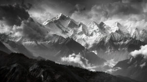 Captivating wallpaper of a black and white mountainscape showcasing snow capped peaks piercing through the clouds amidst rugged terrain