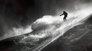 A captivating wallpaper featuring a snowboarder speeding down a steep couloir in black and white with spraying snow in their path
