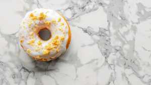 A minimalist design featuring a single donut with white frosting and gold flakes, on a marble surface