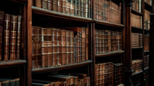 An old towering bookcase made of dark wood adorned with leather bound books nestled in a softly lit room